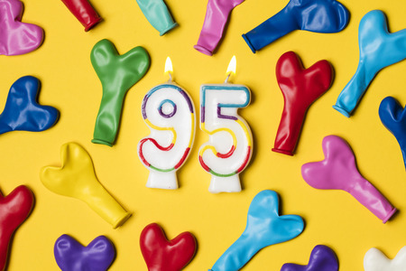 Number 95 candle with party balloons on a bright yellow backgroundの写真素材
