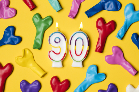 Number 90 candle with party balloons on a bright yellow backgroundの写真素材
