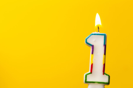 Number 1 birthday celebration candle against a bright yellow backgroundの写真素材