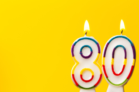 Number 80 birthday celebration candle against a bright yellow backgroundの写真素材