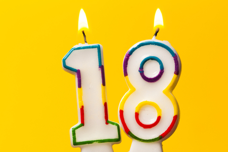 Number 18 birthday celebration candle against a bright yellow backgroundの写真素材