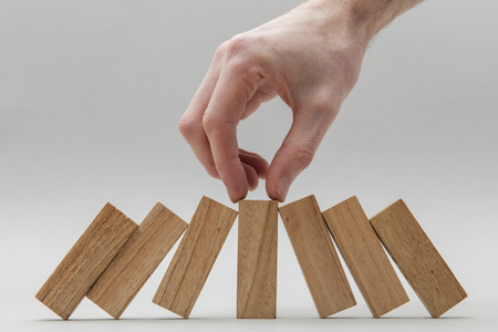 Male hand stopping wooden blocks falling overの写真素材