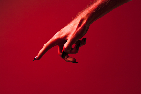 Halloween red devil monster hand with black fingernails against a red backgroundの写真素材