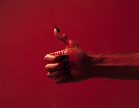 Halloween red devil monster hand with black fingernails against a red backgroundの写真素材