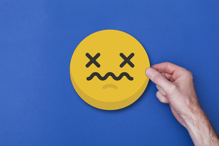 Male hand holding a emoji emoticon unhappy smiley head iconの写真素材