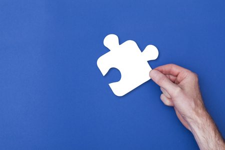 male hand holding a puzzle piece icon symbol against a blue backgroundの写真素材