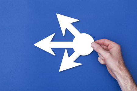 male hand holding an multi option arrow icon symbol against a blue background
