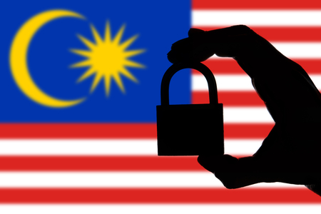 Malaysia security. Silhouette of hand holding a padlock over national flagの写真素材