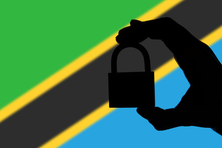 Tanzania security. Silhouette of hand holding a padlock over national flagの写真素材