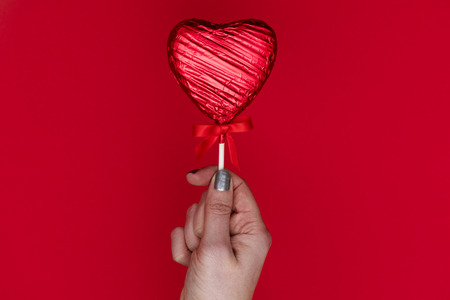 Valentiness day gift. Female hand holding a heart shaped loll against a red backgroundの写真素材