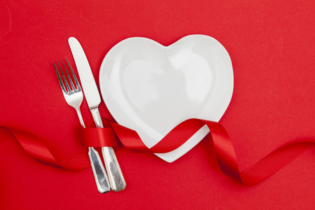 Valentine's day dinner concept. Heart shaped plate with knife and fork on a red backgroundの写真素材