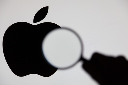 LONDON, UK - MAY 15th 2017: Apple investigation concept. Silhouette of a hand holding a magnifying glass infront of the apple logoのeditorial素材