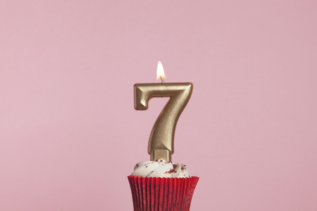 Number 7 gold candle in a cupcake against a pastel pink background