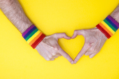 Heart hand with gay pride rainbow flag wristband on a yellow backgroundの写真素材