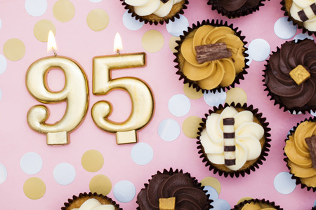 Number 95 gold candle with cupcakes against a pastel pink backgroundの写真素材