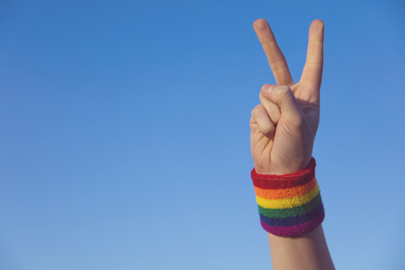 Gay pride concept. Hand making a V peace sign with gay pride LGBT rainbow flag wristbandの写真素材
