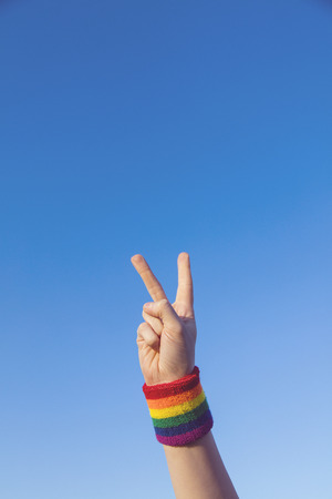 Gay pride concept. Hand making a V peace sign with gay pride LGBT rainbow flag wristbandの写真素材