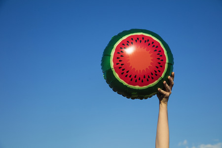 Summer watermelon balloon held in the air against a bright blue summer sky