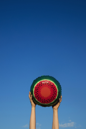 Summer watermelon balloon held in the air against a bright blue summer skyの写真素材