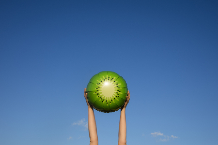 Summer kiwi fruit balloon held in the air against a bright blue summer skyの写真素材