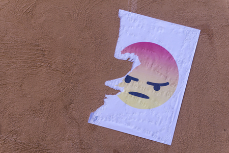 Angry emoji character printed onto paper and stuck on a wall