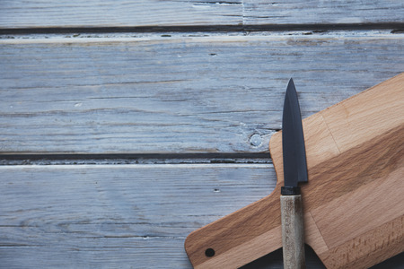 Wooden chopping board and knife on a rustic wood plank background