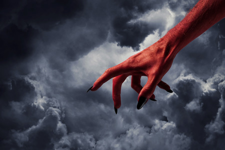 Halloween red devil monster hand with black fingernails against a dark skyの写真素材