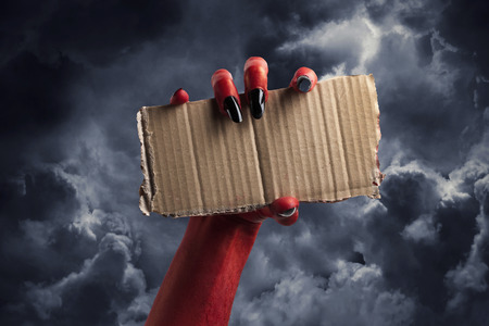 Halloween red devil monster hand with black fingernails against a dark skyの写真素材