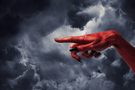 Halloween red devil monster hand with black fingernails against a dark skyの写真素材