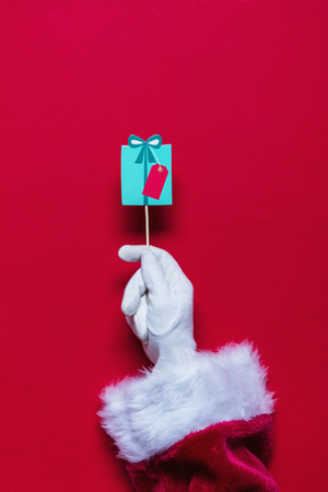 Santa Claus Christmas hand holding a gift against a red backgroundの写真素材