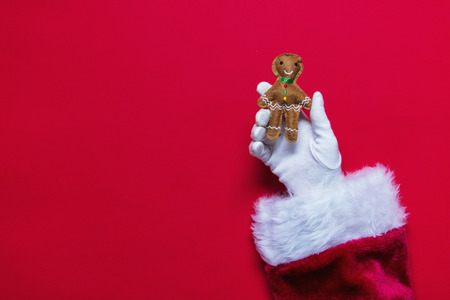 Santa Claus Christmas hand holding a gingerbread decoration against a red background