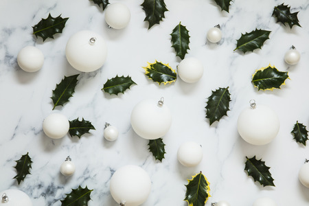 Christmas layout made from festive holly leaves on a white marble backgroundの写真素材