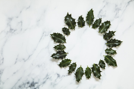 Christmas layout made from festive holly leaves on a white marble background