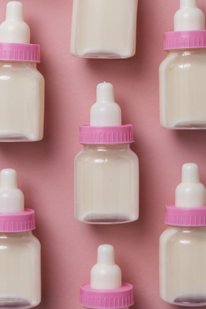 Baby bottles with milk on a pastel pink background