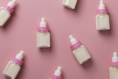 Baby bottles with milk on a pastel pink background