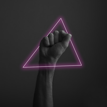 Raised clenched fist against a dark background with abstract neon light glowの写真素材
