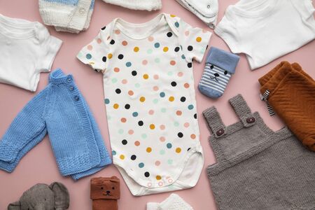 Cute baby clothes layout on a pastel pink background