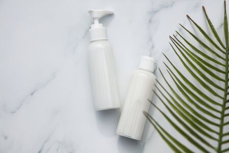 Skincare and cosmetic products on a marble background with tropical palm leaf