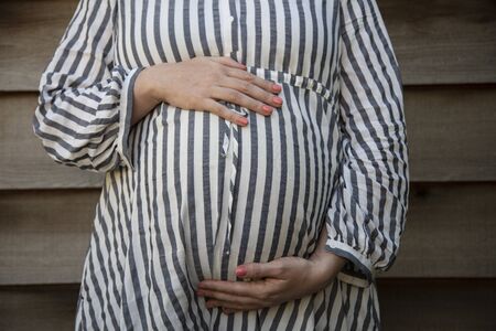 A pregnant woman holding her baby bump stood against a plain background