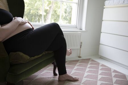 A prgnant woman holding her baby bump whilst relaxing on a chair