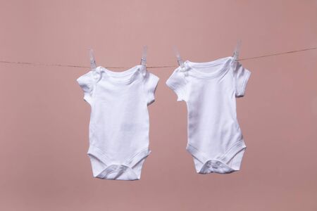 White baby body suit hanging from a line against a pink backgroundの写真素材