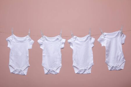 White baby body suit hanging from a line against a pink background