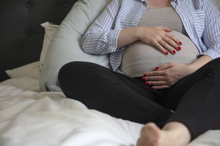 A young pregnant woman resting at home sitting on a bed. Expectant motherの写真素材