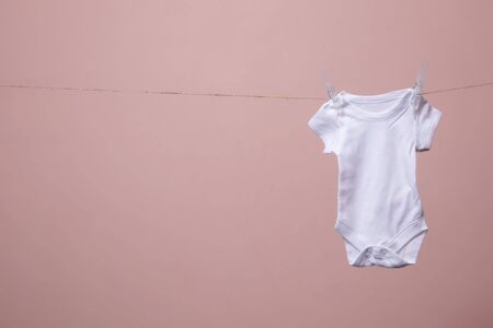 White baby body suit hanging from a line against a pink backgroundの写真素材