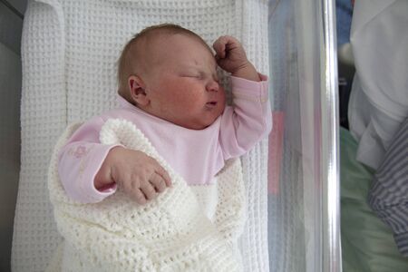 A cute one day old baby asleep in a hospital cot