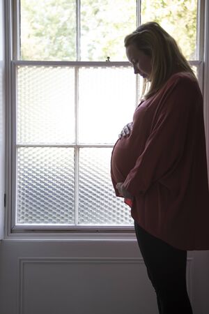 Silhouette of a prgnant woman standing infront of a window