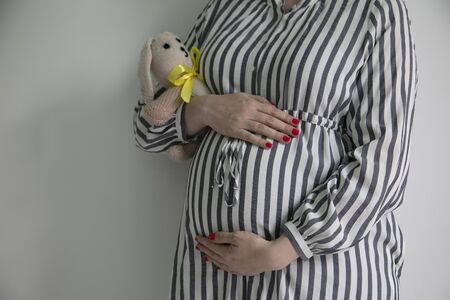 A pregnany woman holding her tummy and a bunny teddy bearの写真素材