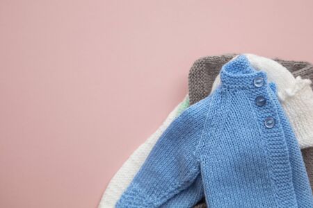 Cute knitted baby clothes layout on a pastel pink background