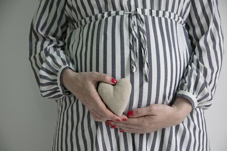 A pregnant woman holding a heart shape in front of here baby bump