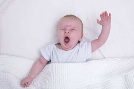A tired young baby under a blanket yawningの写真素材